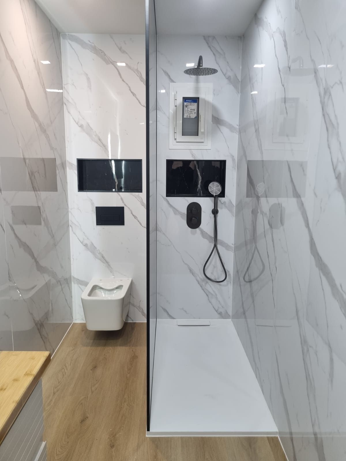 Baño moderno con azulejos de aspecto mármol, ducha, inodoro y estanterías empotradas.