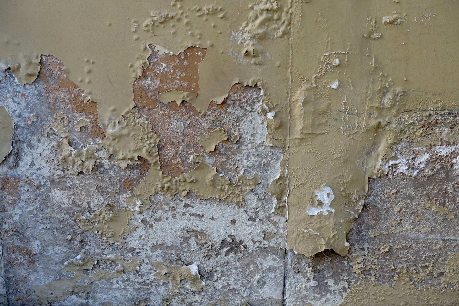 Peinture jaune écaillée sur un mur, révélant des couches blanches et grises en dessous