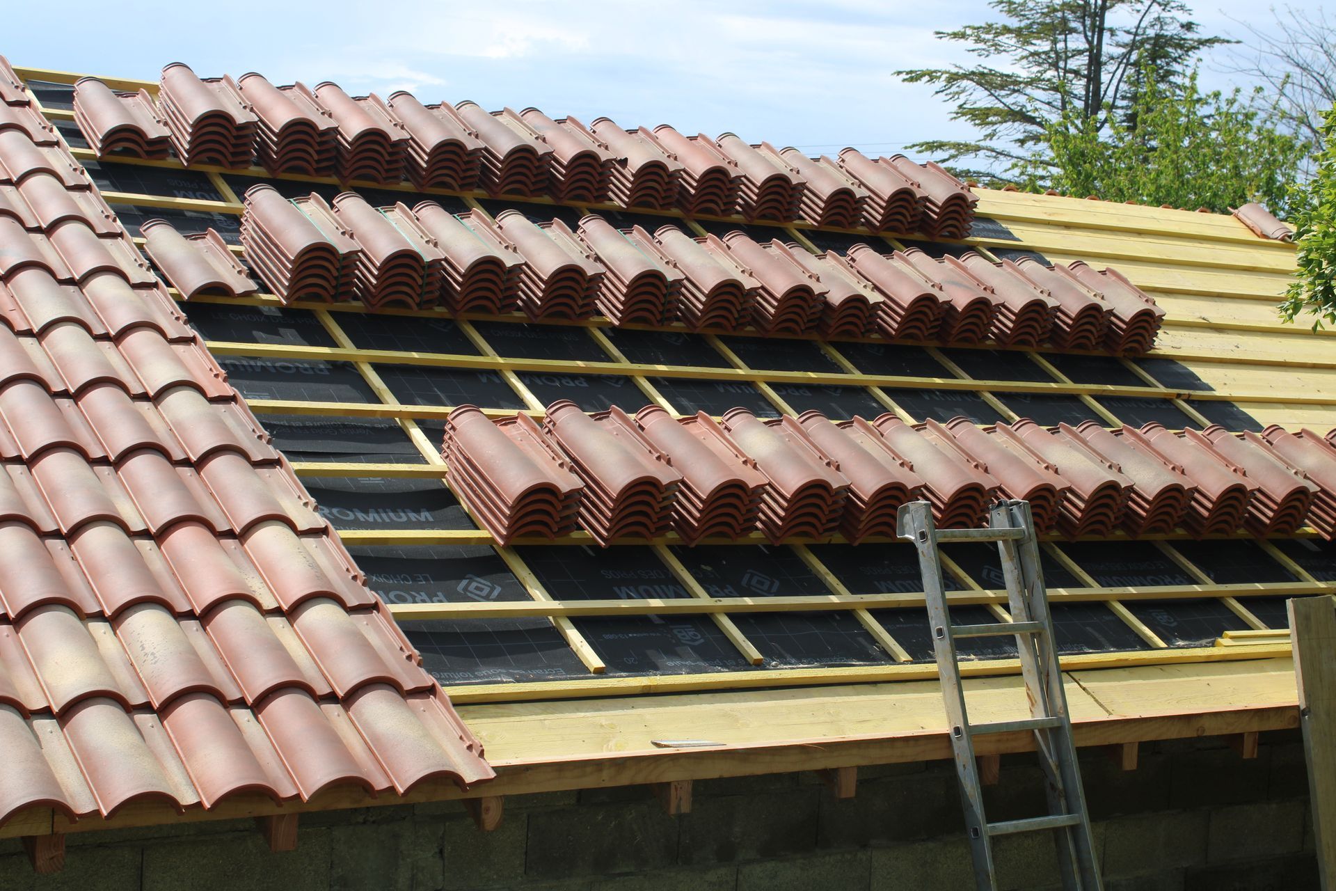 Toiture en construction avec tuiles de terre cuite rouge, charpente en bois et échelle