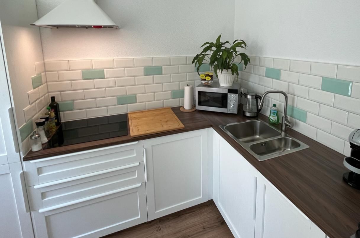 Eine Küche mit weißen Schränken, einer Spüle, einer Mikrowelle und einem Herd.