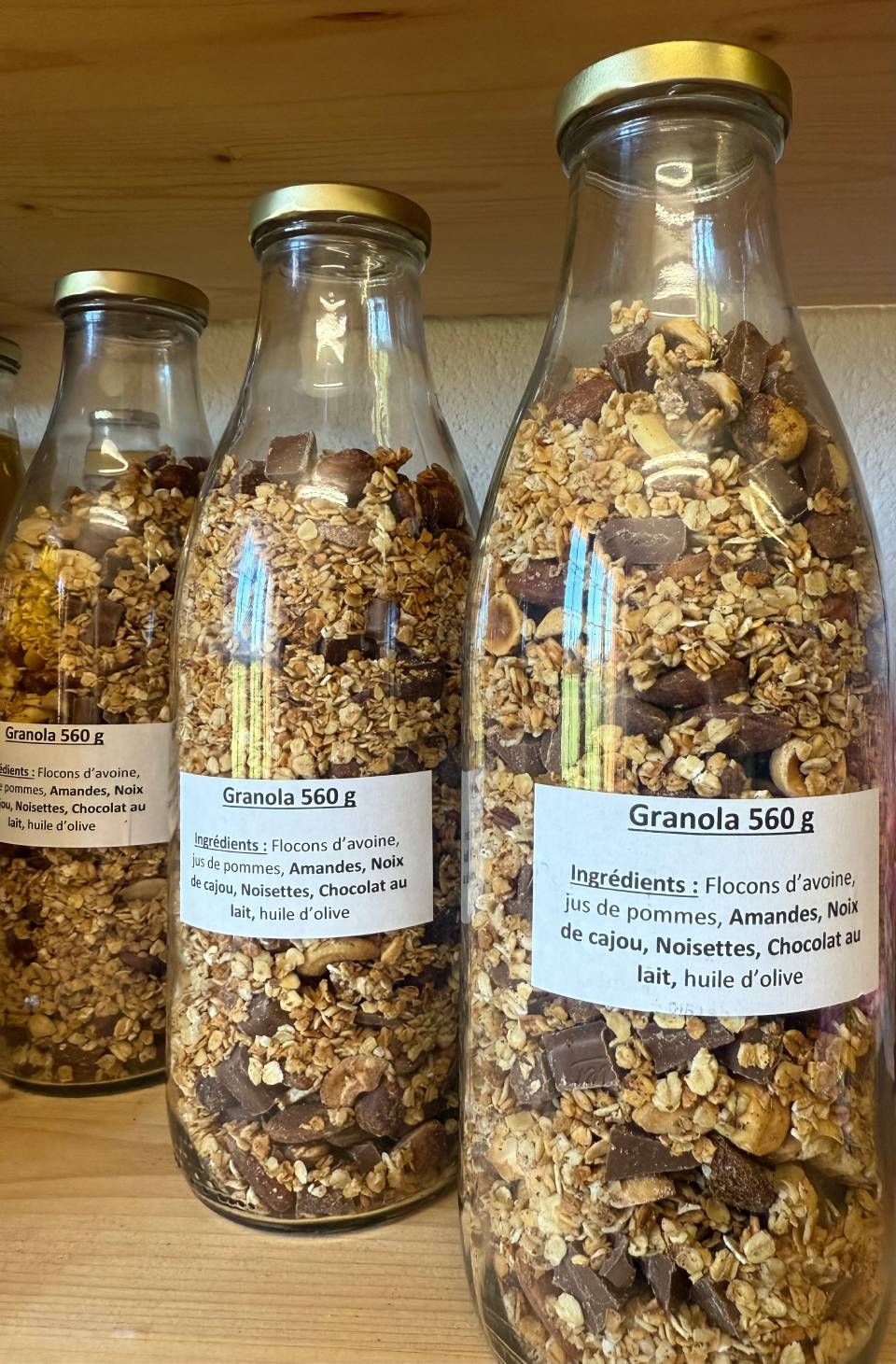 Trois bouteilles de granola sont posées sur une étagère en bois.