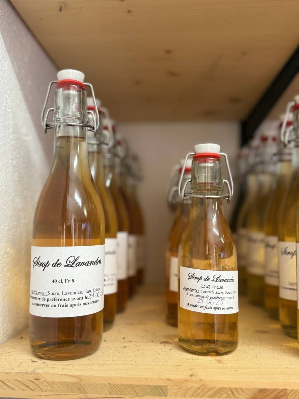 Une rangée de bouteilles de sirop est posée sur une étagère en bois.