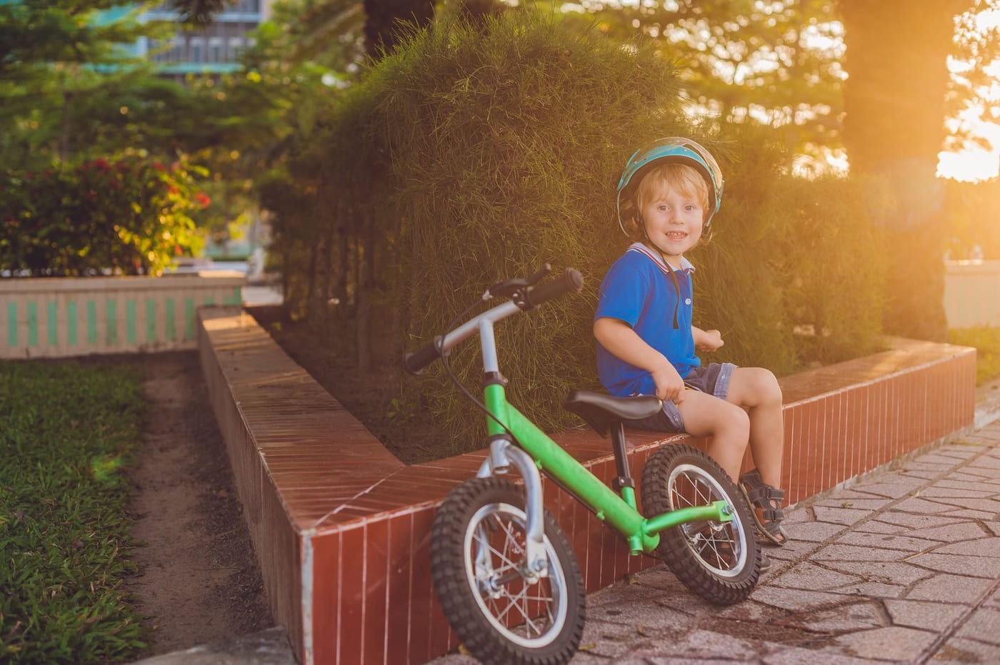 Un niño pequeño está sentado en una bicicleta de equilibrio verde.