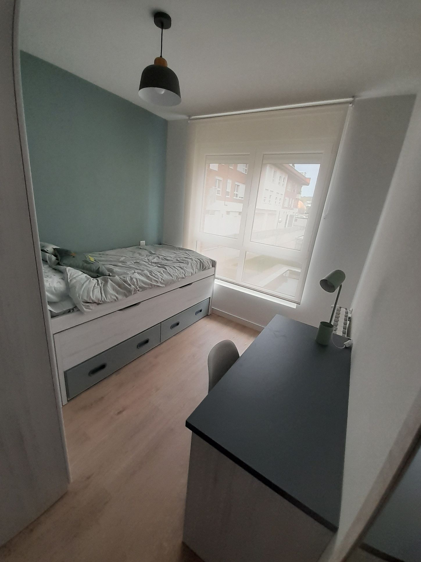 Un dormitorio con cama, escritorio, lámpara y ventana.