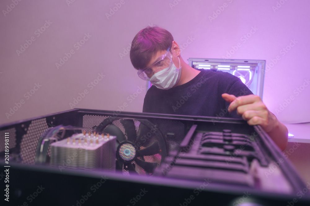 Eine Person mit Maske arbeitet an einem offenen Desktop-Computer mit violetter Beleuchtung.