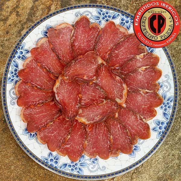 Lonchas de cerdo ibérico curado dispuestas en plato estampado, con pegatina de la marca.