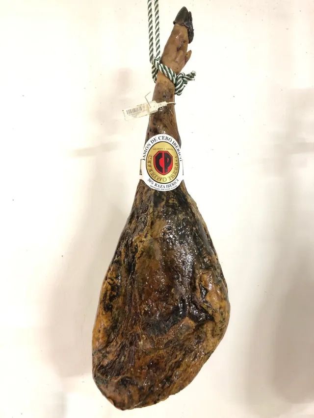 Jamón ibérico entero, de color marrón oscuro y de forma colgante, con etiqueta circular.