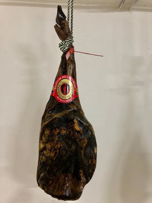 Jamón ibérico entero oscuro colgado, atado con cuerda y etiqueta.