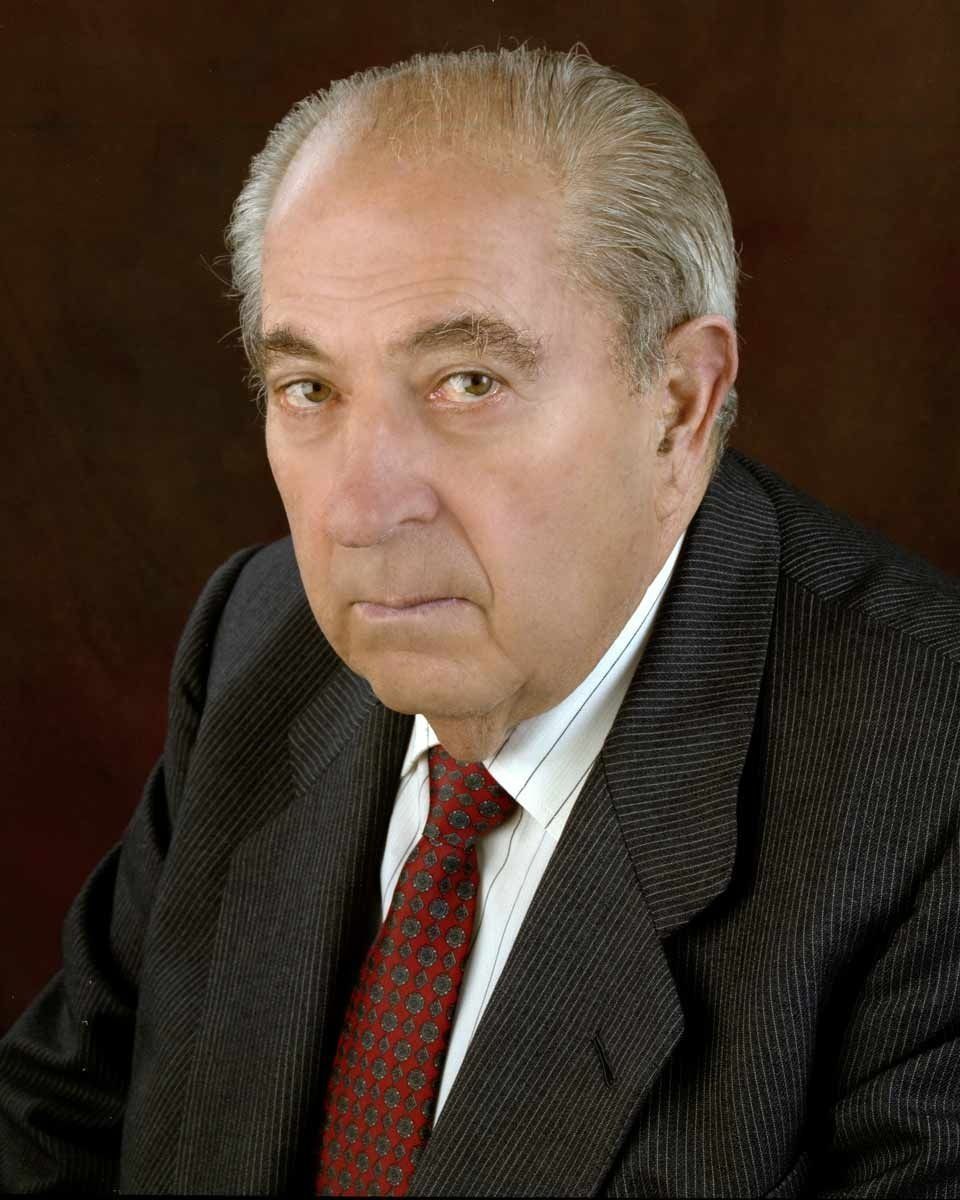 Hombre con traje y corbata mirando hacia adelante con una expresión seria.