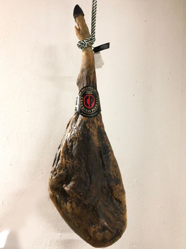 Pata de jamón serrano colgante, de color marrón oscuro, atada con cuerda y etiquetada.
