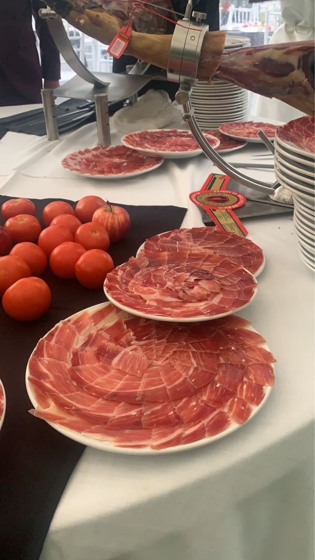 Lonchas de jamón en platos, tomates cherry y jamón. Mesa con mantel blanco.