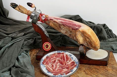 Un jamón curado sobre un soporte de madera, carne cortada en rodajas en un plato.