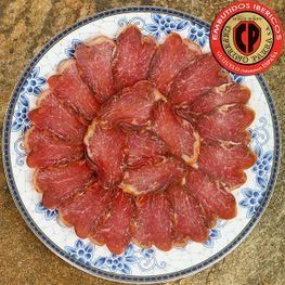Lomo de cerdo ibérico curado lonchas, dispuesto en forma circular sobre un plato decorativo.