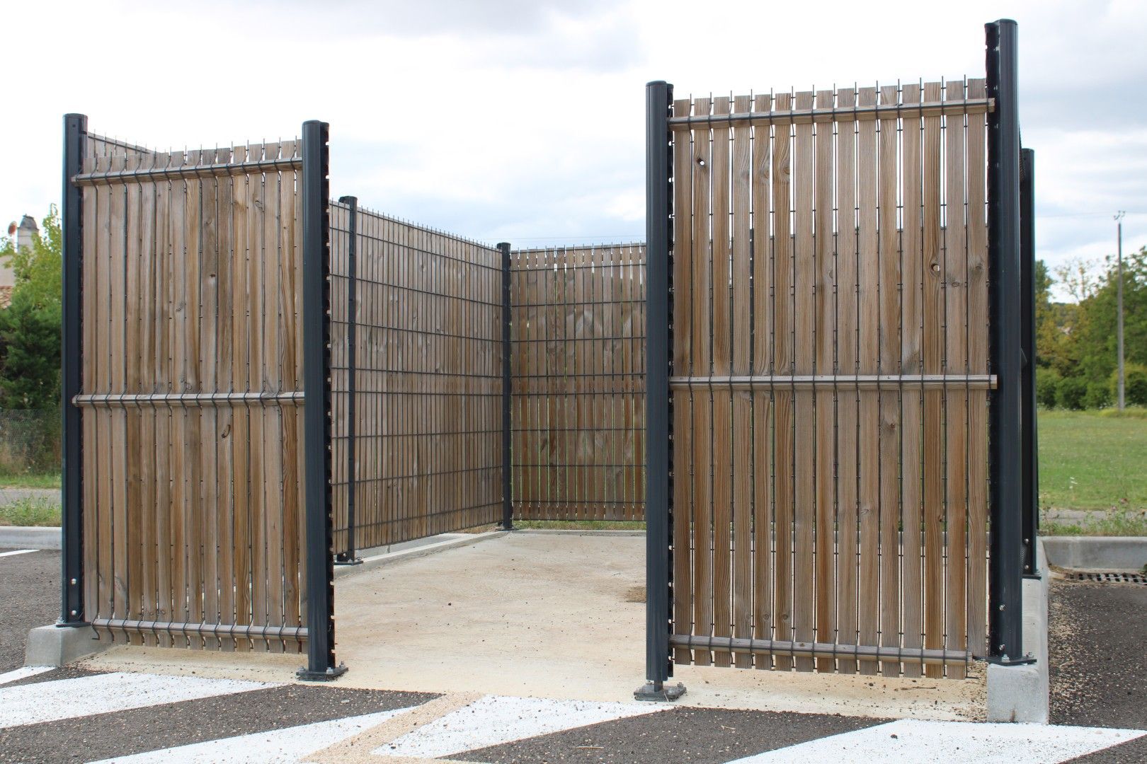 Enclos ouvert en bois de style bambou, avec des poteaux noirs, sur une dalle de béton à l’extérieur