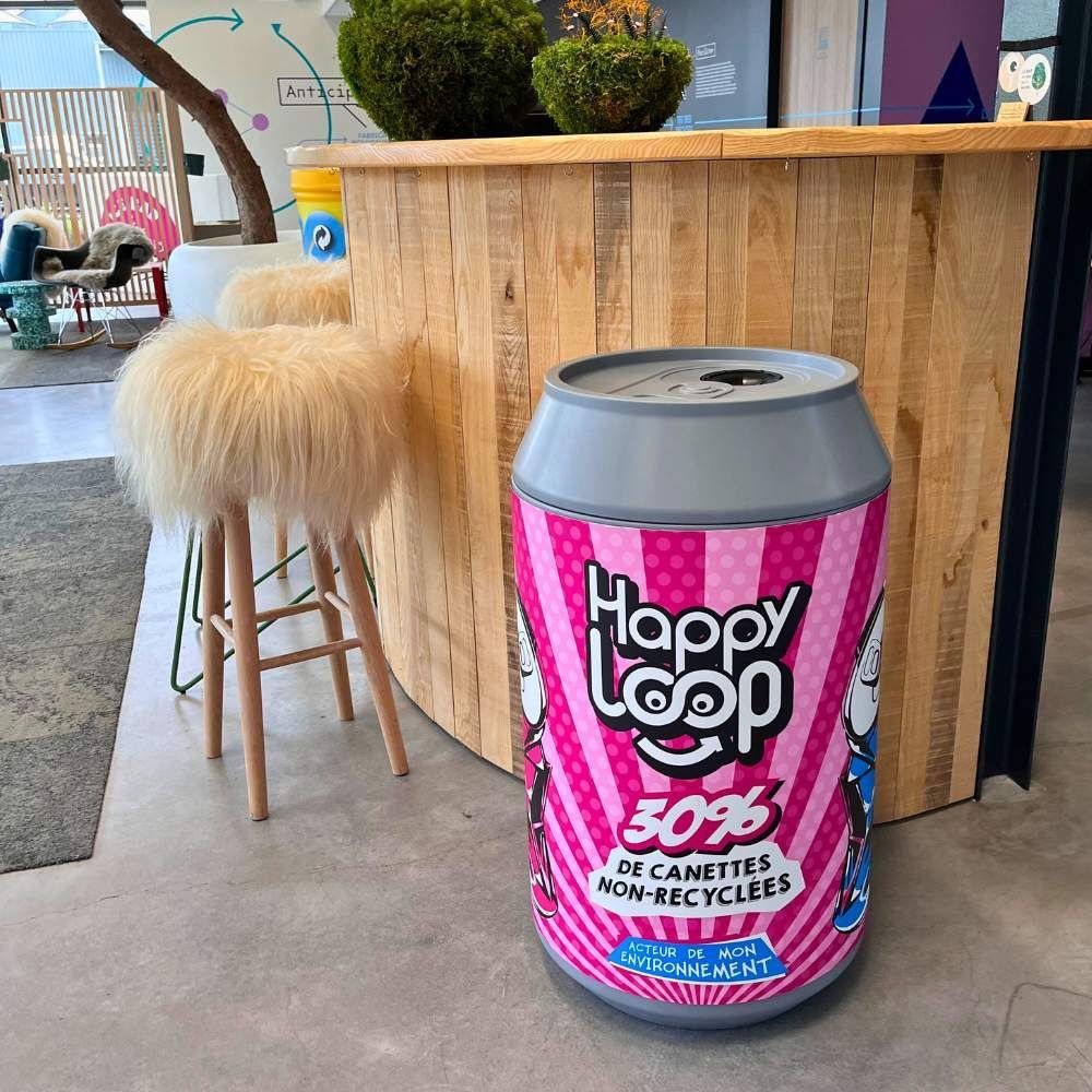 Poubelle de recyclage rose Happy Loop à côté d’un comptoir en bois et d’un tabouret moelleux dans un café