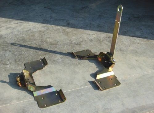 Deux supports métalliques reliés par une sangle noire, posés sur un sol en béton, l’un muni d’une barre verticale servant de poignée