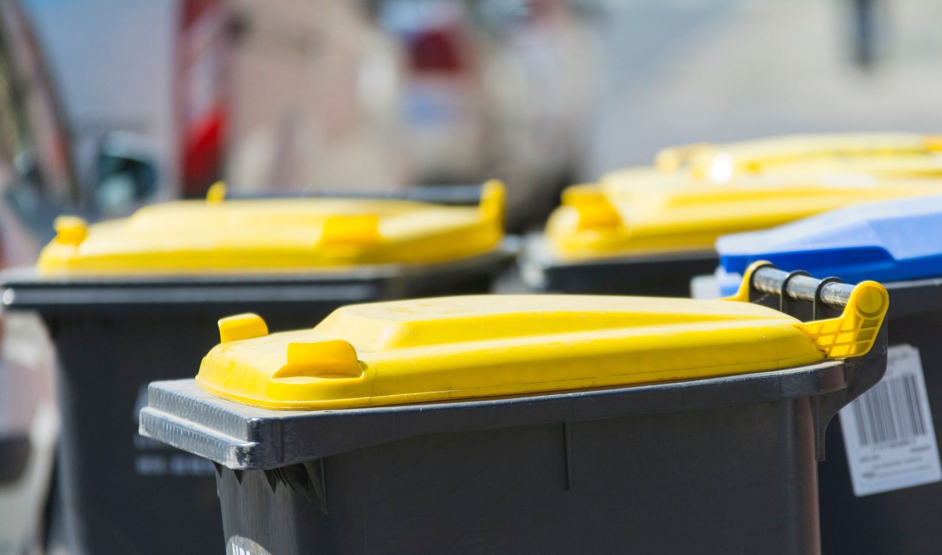 Rangée de poubelles gris foncé aux couvercles jaune vif le long d’une rue