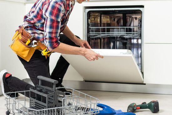 Un hombre está arreglando un lavavajillas en una cocina.