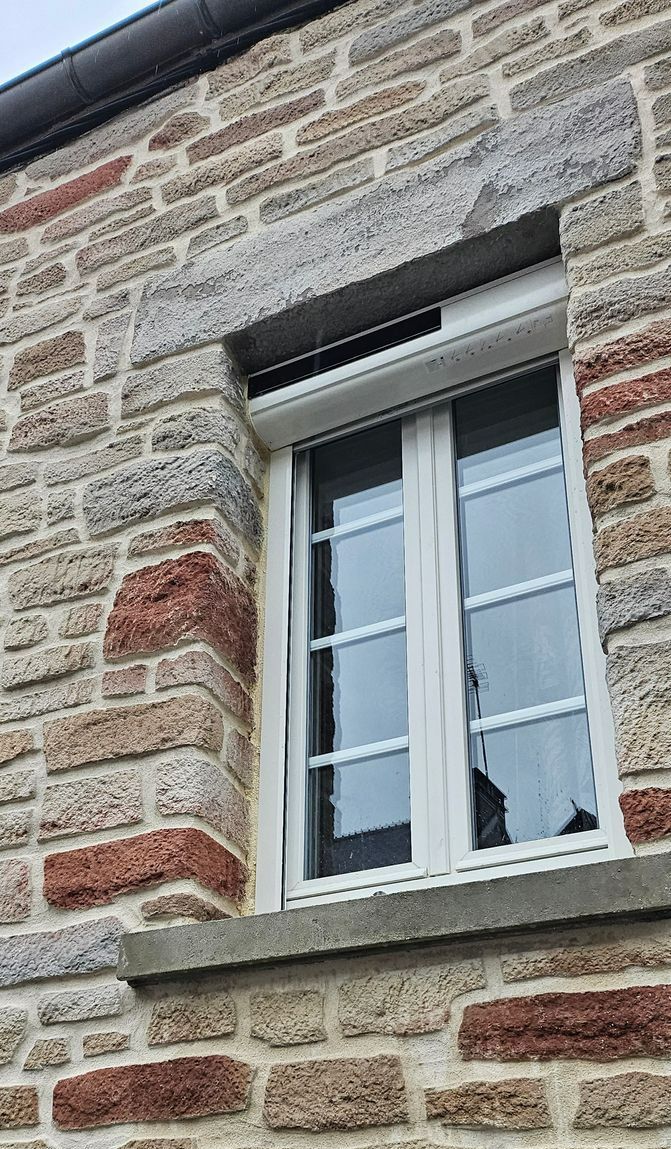 Fenêtre blanche sur un mur en pierres apparentes.