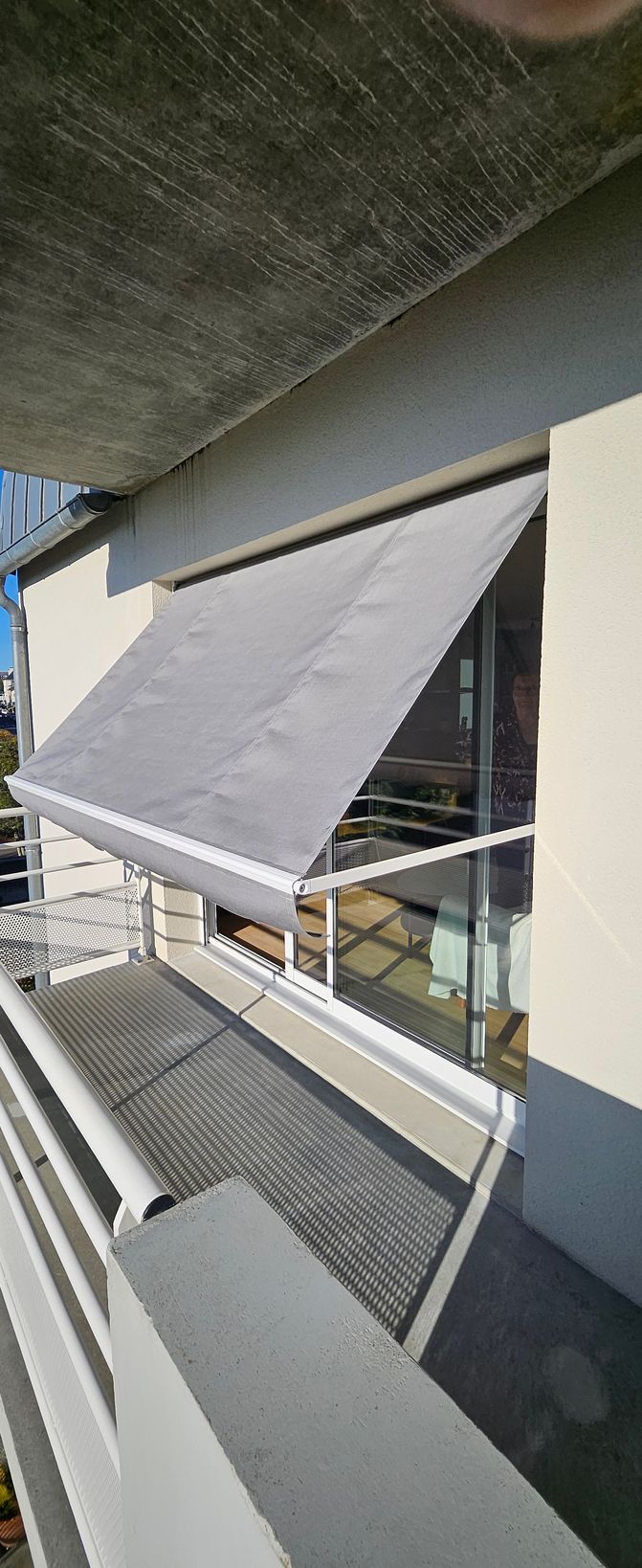 Un auvent gris s'étendant d'un bâtiment au-dessus d'une fenêtre, vu depuis un balcon avec une balustrade.