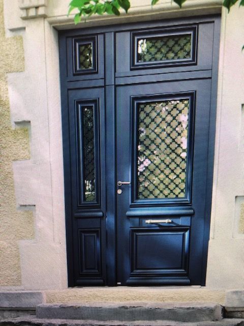 Porte d'entrée noire avec vitres en verre au plomb et moulure décorative dans un cadre en grès.