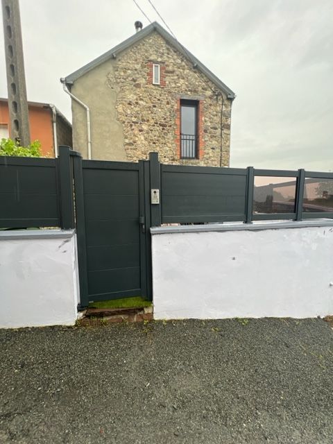 Portail gris foncé devant une maison en pierre avec une clôture assortie sur un mur blanc.