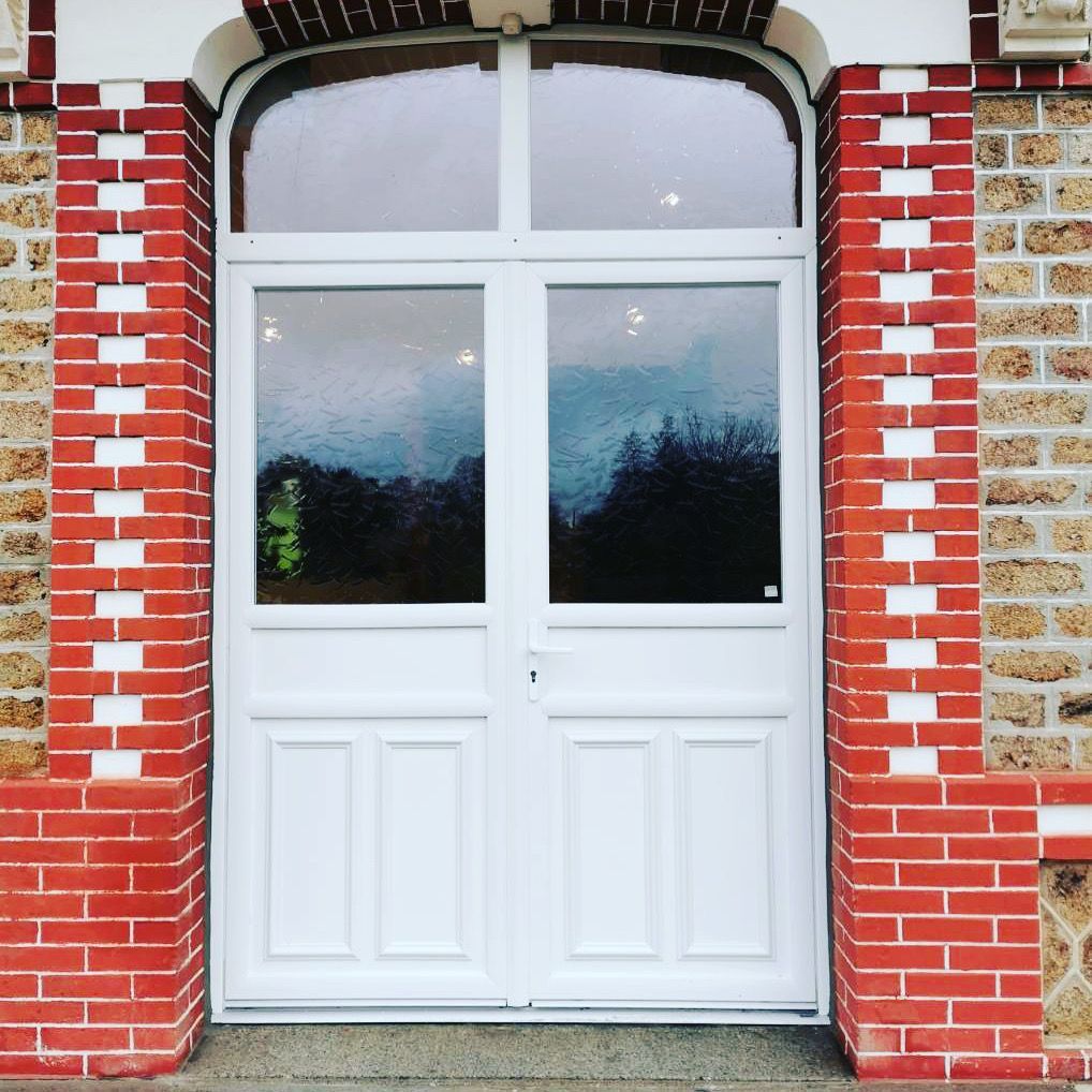 Portes doubles blanches avec panneaux de verre, cadre en briques rouges, dessus arqué, décor extérieur.