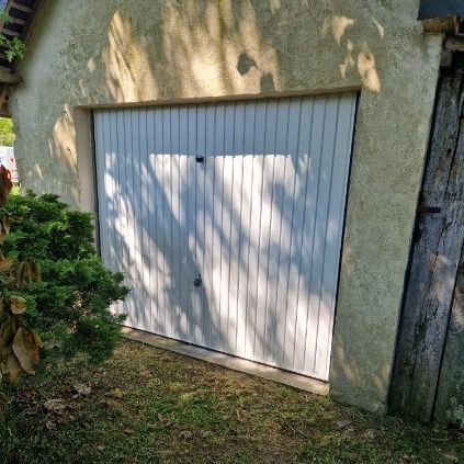 Garage avec porte blanche, situé dans un bâtiment en stuc; partiellement ombragé avec des ombres.