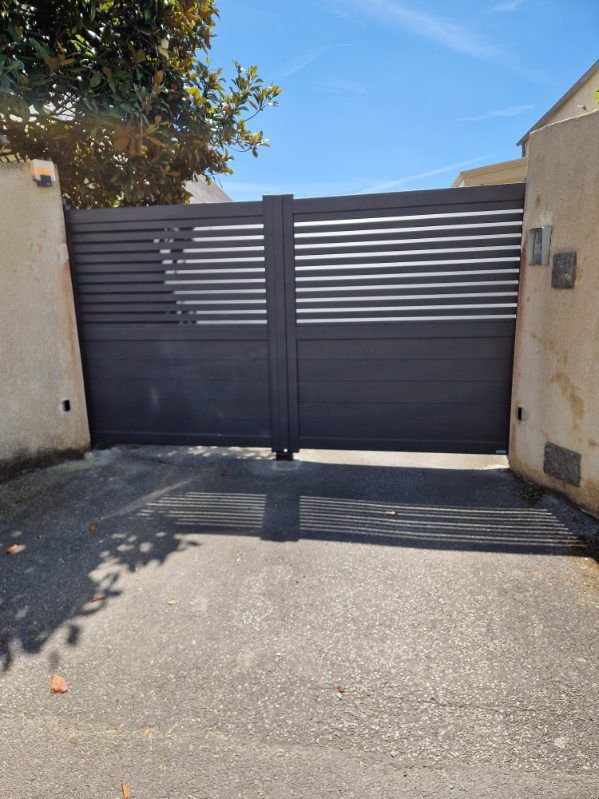 Portail d'allée gris foncé à lattes horizontales entre murs beiges; allée asphaltée.