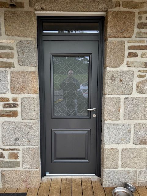 Porte grise avec panneau de verre encastré dans un mur en pierre.