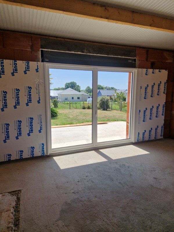 Vue intérieure d'une pièce inachevée avec une porte vitrée à cadre blanc menant à une cour extérieure.