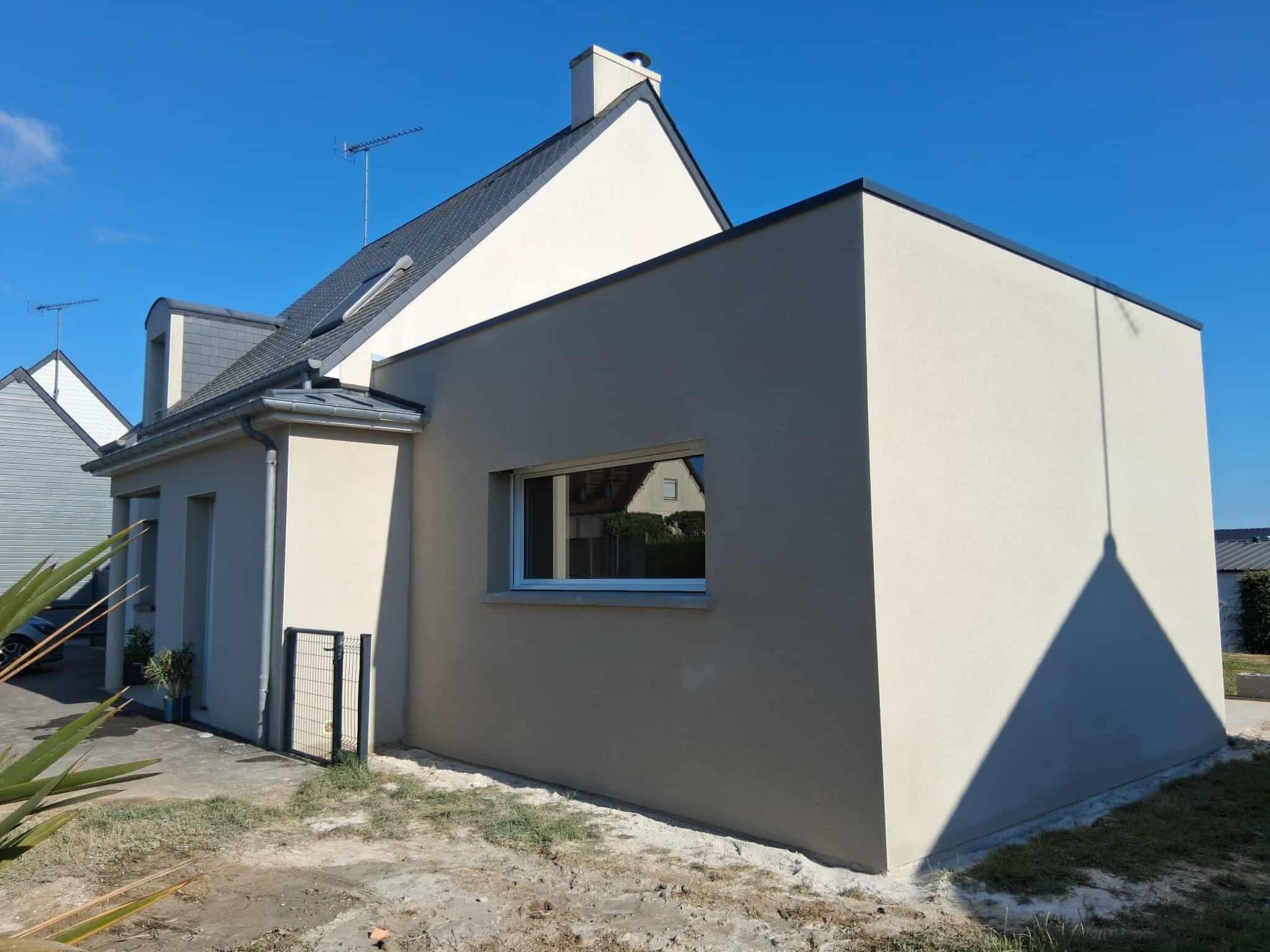 Maison beige avec extension, ciel bleu, herbe et une fenêtre.