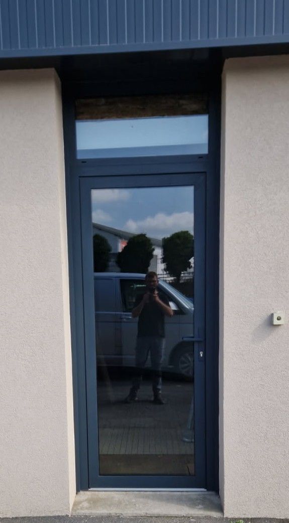 Porte grise avec fenêtre supérieure, verre réfléchissant, mur beige, garniture bleue.