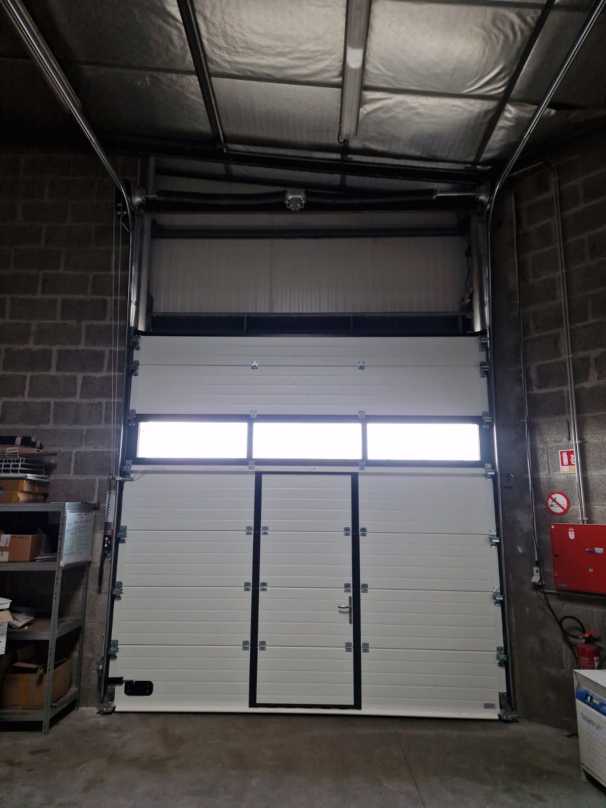 Porte basculante industrielle blanche, ouverte à l'intérieur de l'entrepôt.