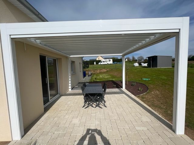 Pergola blanche sur patio, avec une table et des chaises, à côté d'une maison avec portes coulissantes, à l'extérieur par une journée ensoleillée.