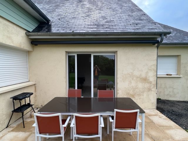 Un patio avec une table et des chaises sous un auvent rétractable devant une maison avec une porte coulissante en verre.