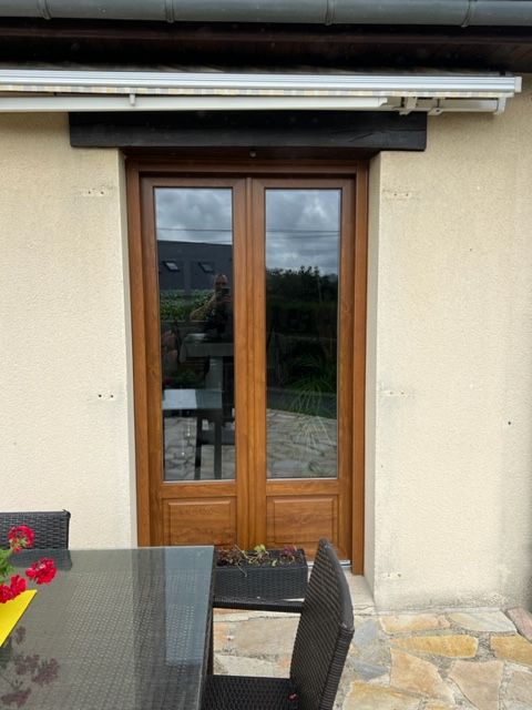 Portes doubles marron vitrées, sous un store rétractable, sur un mur extérieur beige. Terrasse extérieure avec table et chaises.