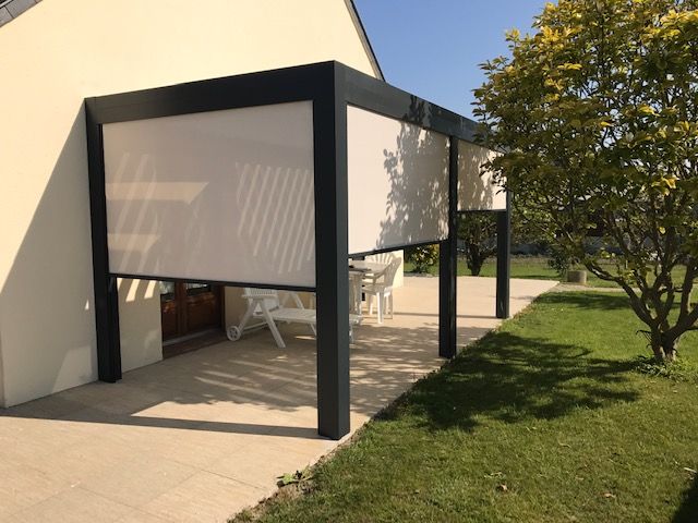Pergola moderne avec store blanc rétractable, attachée à une maison beige par une journée ensoleillée.