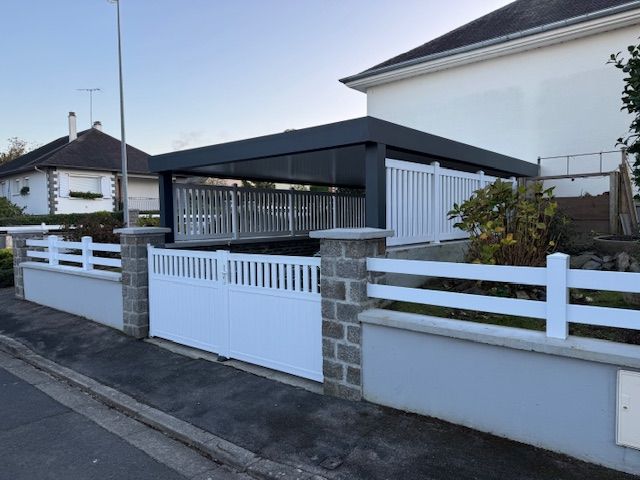 Un portail et une clôture blancs entourent une maison avec un abri voiture ; extérieur gris et blanc, lumière du jour éclatante.