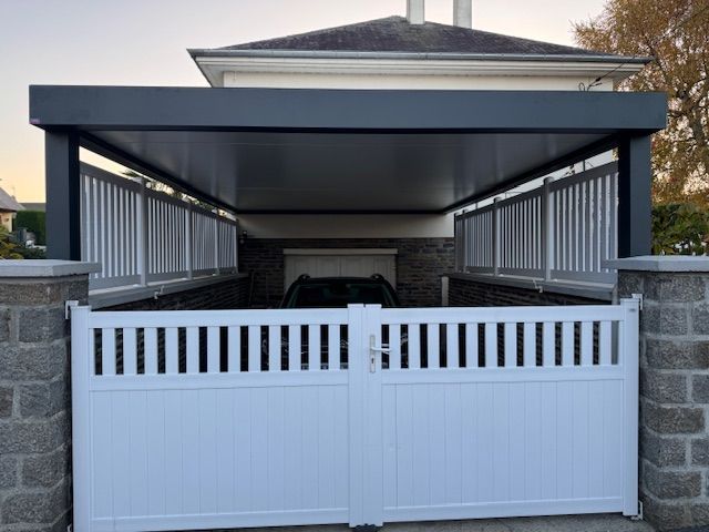 Abri d'auto blanc fermé avec toit gris, piliers en briques et une voiture garée à l'intérieur.