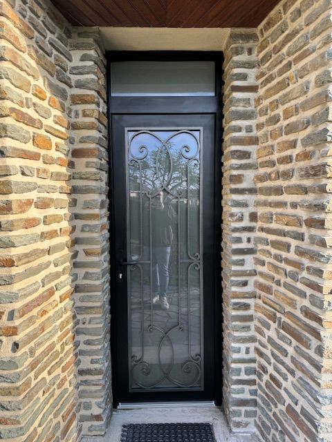 Porte d'entrée à cadre noir avec design en verre et fer forgé, encastrée dans un mur de briques.