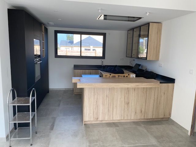 Cuisine moderne avec armoires noires et en bois clair, îlot et fenêtre.