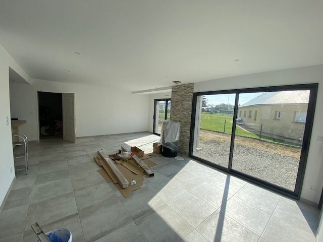 Intérieur d'une maison moderne avec de grandes fenêtres, un sol en carrelage gris clair et une colonne en pierre.