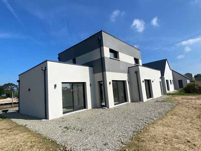 Maison moderne à deux étages avec extérieur gris et blanc, grandes fenêtres et aménagement paysager en gravier sous un ciel bleu.