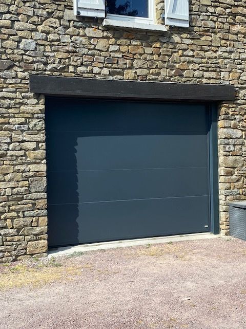 Porte de garage gris foncé dans un bâtiment en pierre.