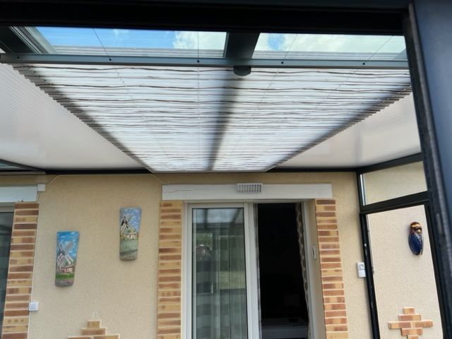 Véranda avec toit rétractable, murs de couleur claire, garniture en brique et porte coulissante, avec décoration murale.