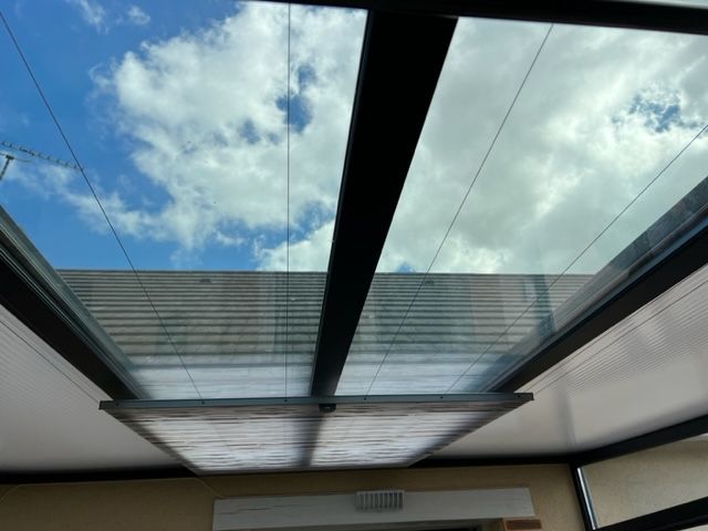 Toit en verre avec ciel bleu et nuages visibles. Cadres noirs avec éclairage intérieur.