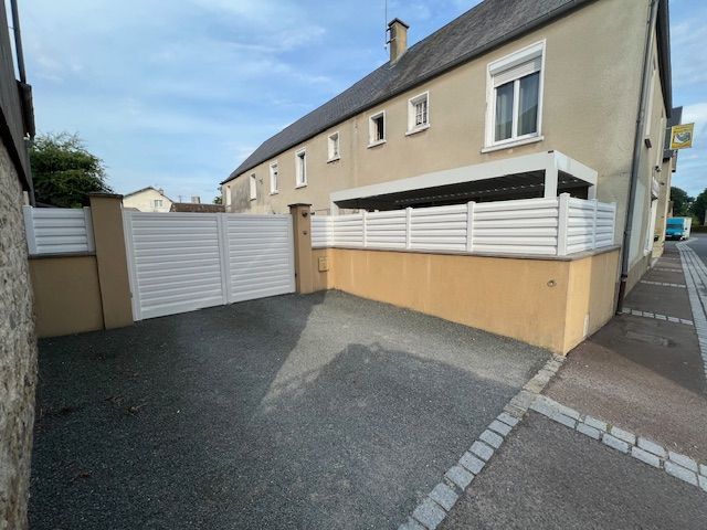 Une clôture blanche et un portail entourent une allée avec un bâtiment en arrière-plan sur une rue pavée.