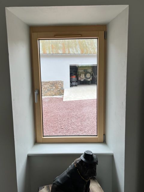 Fenêtre avec vue sur un garage et gravier rouge ; figure sur le rebord.