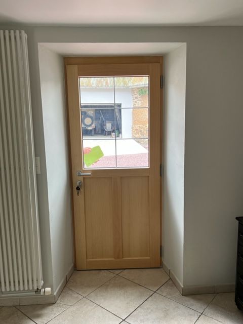 Porte extérieure en bois avec panneaux de verre encastrés dans un mur blanc, menant à un espace extérieur.